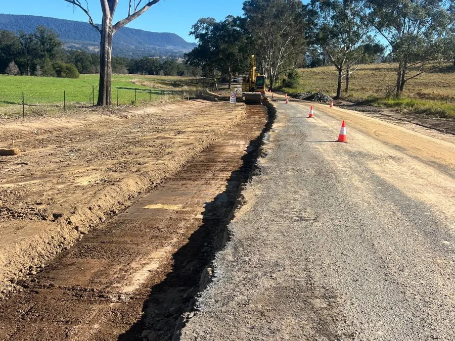 Road boxed out for widening, with an excavator working further along