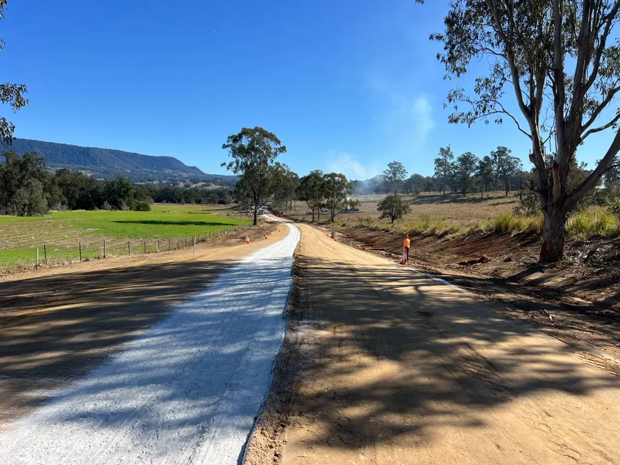 Rural road widening with a stabilised strip and mountains behind
